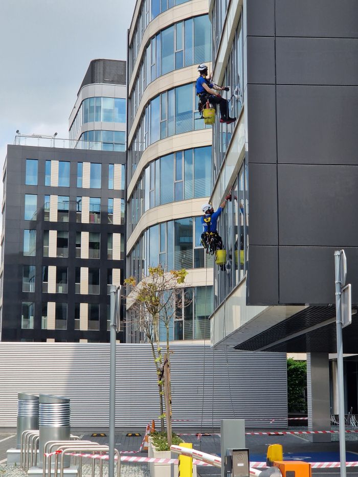 Deux employés nettoient les vitres d’un immeuble de bureaux élevé en milieu urbain.